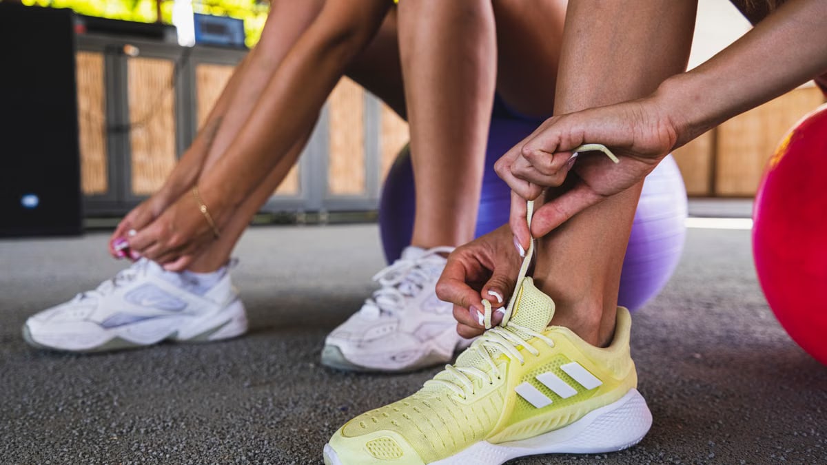 Close-up of women tying shoes on exercise balls, ready for fitness routine.